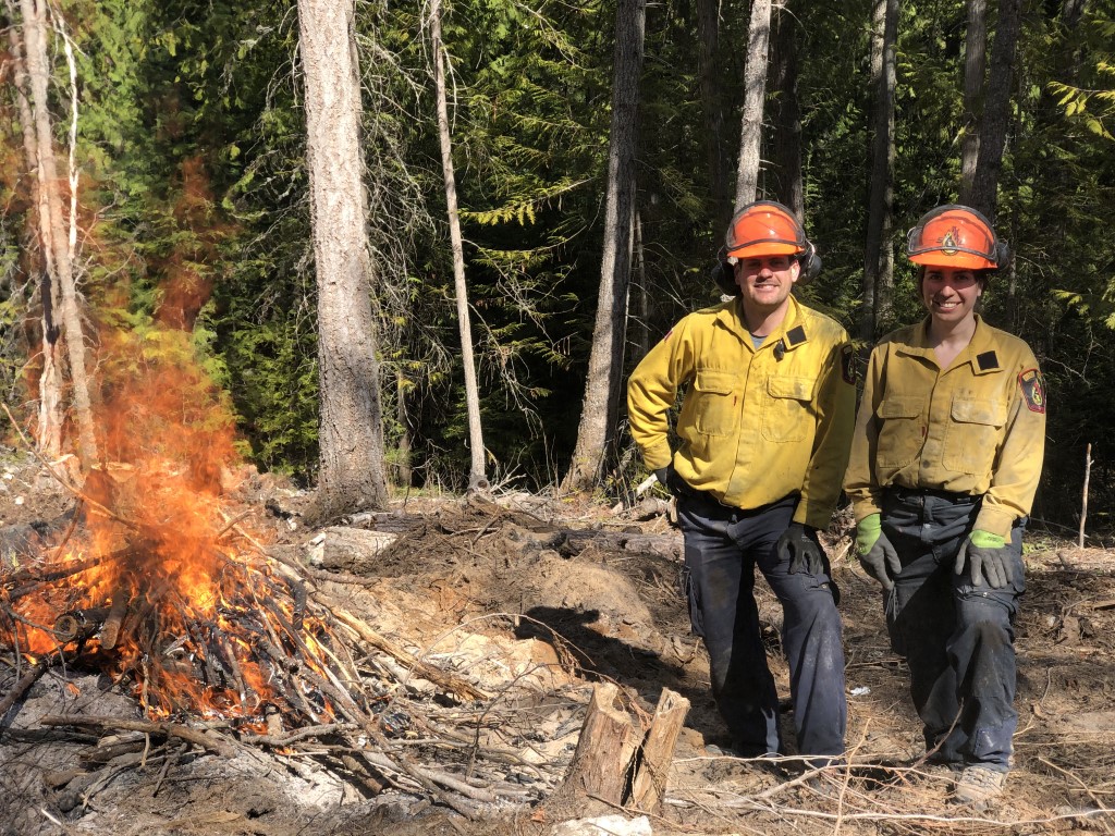 Two forestry workers standing next to a burn pile.