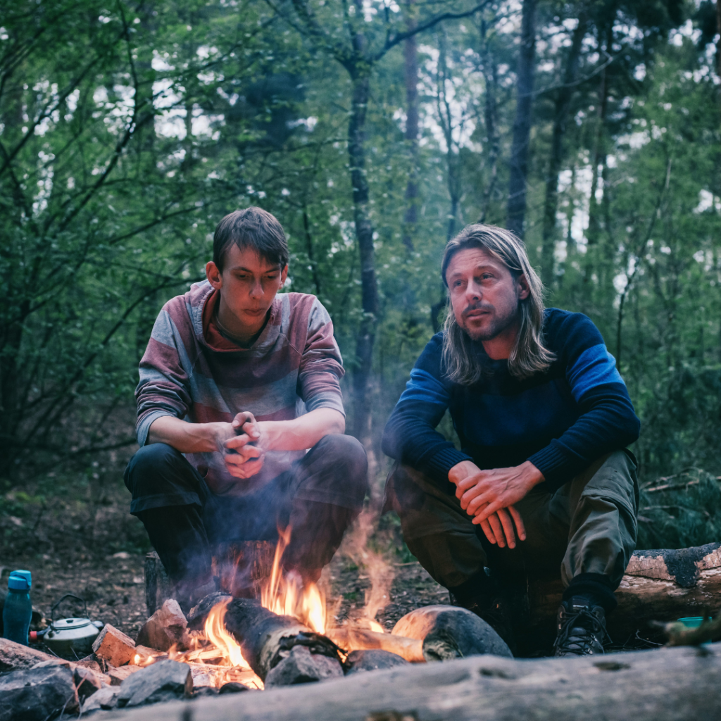 Two men sitting around a campfire in the forest