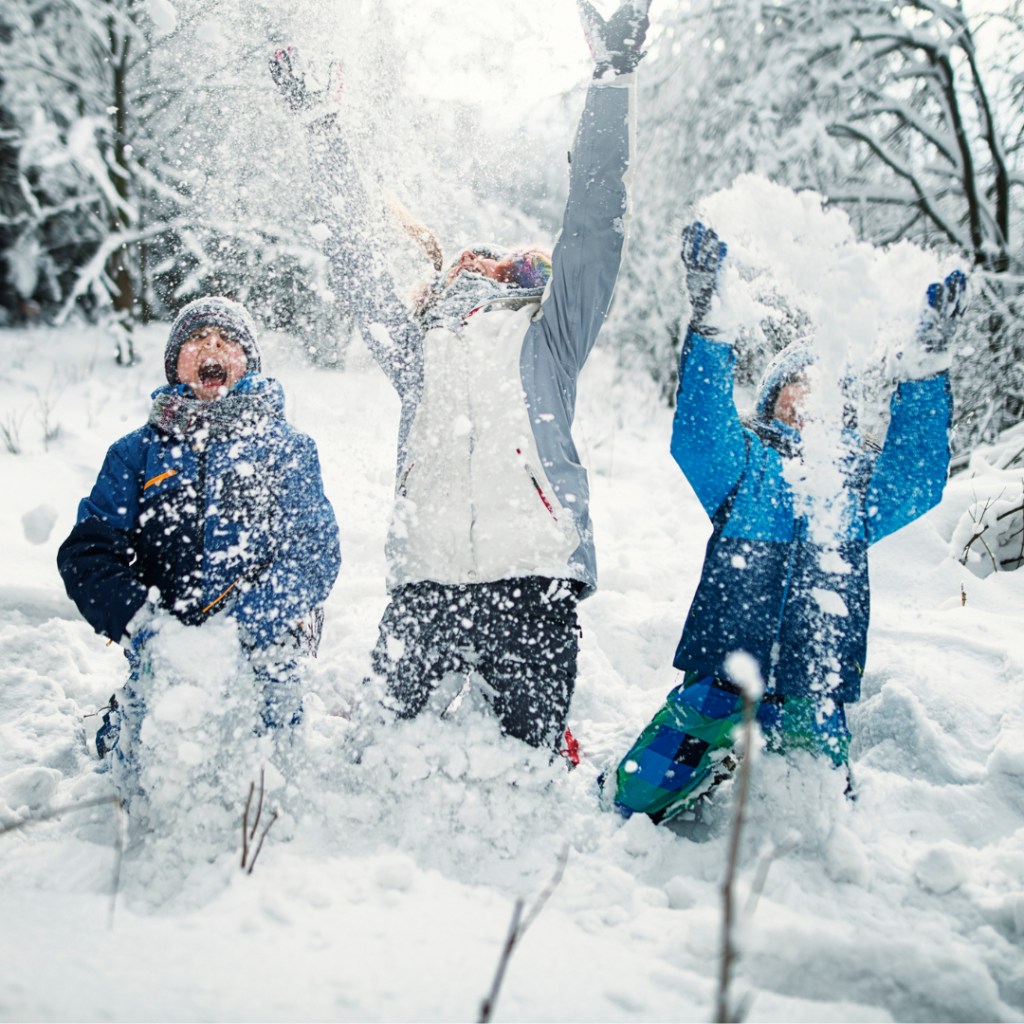 3 young kids kneeling on the ground in the snow. They are throwing the snow up in the air.