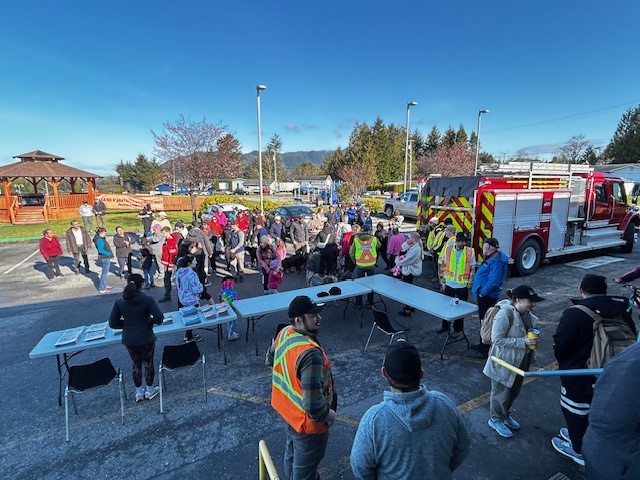 A community of people gather outside on a sunny day near a fire truck to prepare for their High Ground Hike.