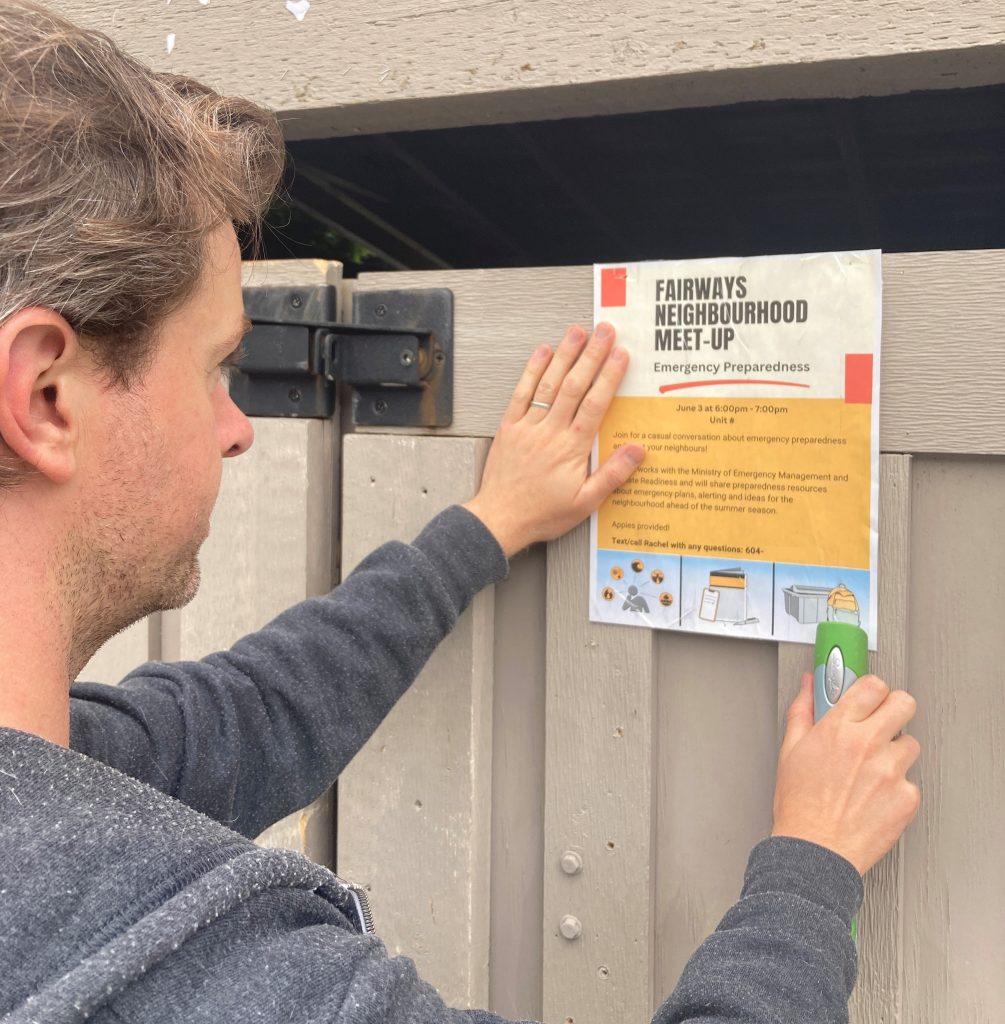 Resident hanging up a neighbourhood meetup poster on a wooden fence.